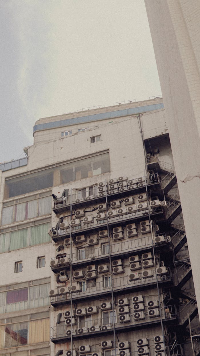 A highrise building with prominent exterior air conditioning units viewed from a low angle.